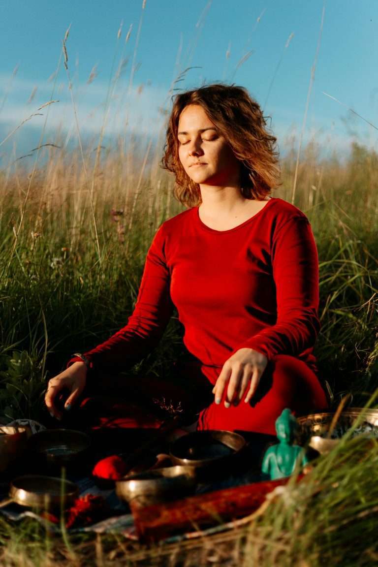 Woman in red practicing meditation in a peaceful outdoor environment with grass and sunlight.